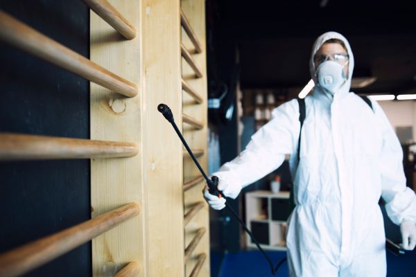 A man in protective gear and a white suit stands with a sprayer, poised to carry out pest control operations effectively.